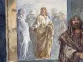 Jezus w złotej szacie przemawia do ludzi, przypominając o głównych prawdach wiary. Obok stoi mężczyzna w brązowym płaszczu.