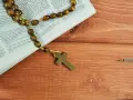 Różaniec na drewnianym stole obok Biblii, przypominający o 10 przykazaniach kościelnych i modlitwie.