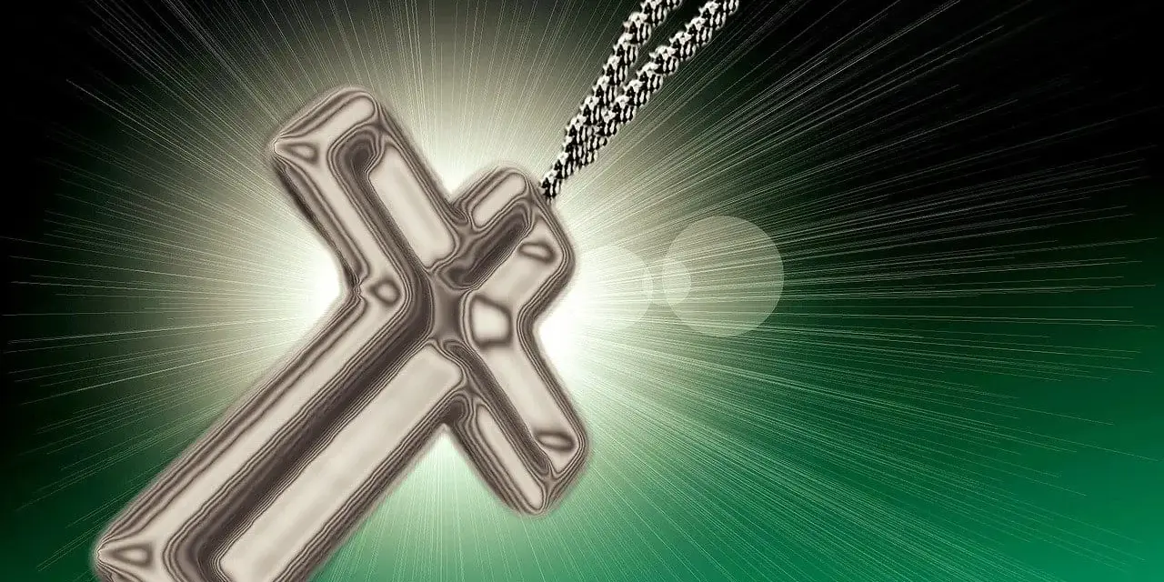 Metalowy krzyż na łańcuszku, symbol wiary i religii w Polsce, emanuje światłem.