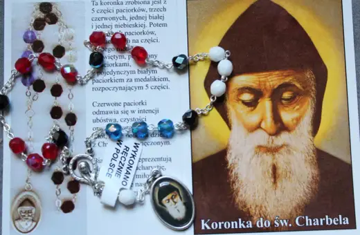 Koronka do św. Charbela z czerwonymi i białymi paciorkami, obok wizerunku świętego.