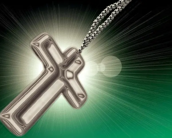 Metalowy krzyż na łańcuszku, symbol wiary i religii w Polsce, emanuje światłem.