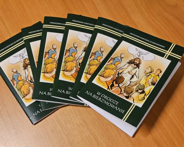 Kilka zielonych książek z ilustracją Jezusa i gołębicy na drewnianym stole.