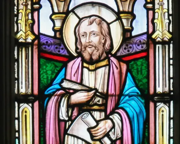 Witraż przedstawia świętego Łukasza z księgą i zwojem, symbolizując jego rolę jako ewangelisty i pisarza.