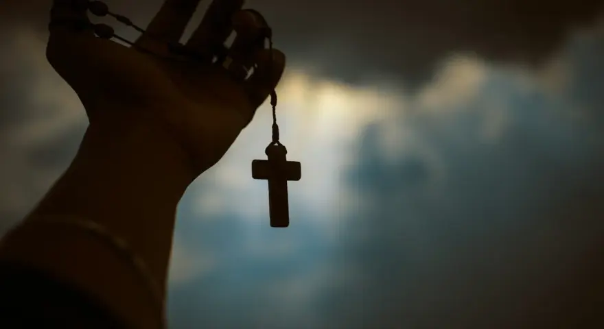 Dłoń trzyma paciorki różańca z krzyżem, symbolizując poszukiwanie prawdy w obliczu niepewności, jak agnostycyzm.