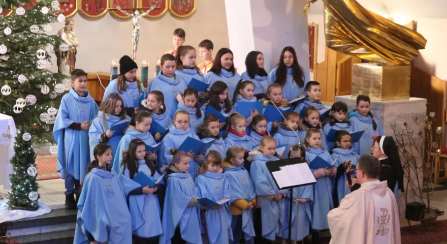 Dzieci w błękitnych strojach tworzą schola, śpiewając w kościele przy choince.