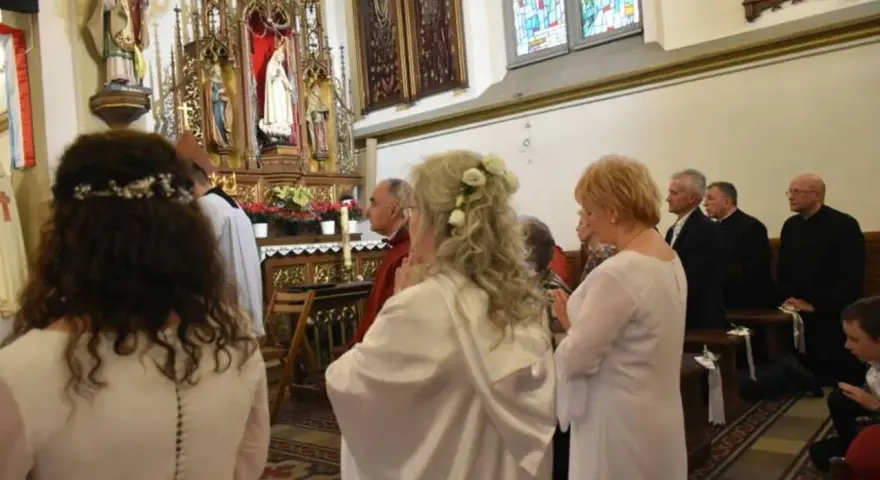 Uroczystość w kościele. Kobieta w białej sukni, z kwiatami we włosach, klęczy. To moment konsekracji, ważny dla dziewicy konsekrowanej.