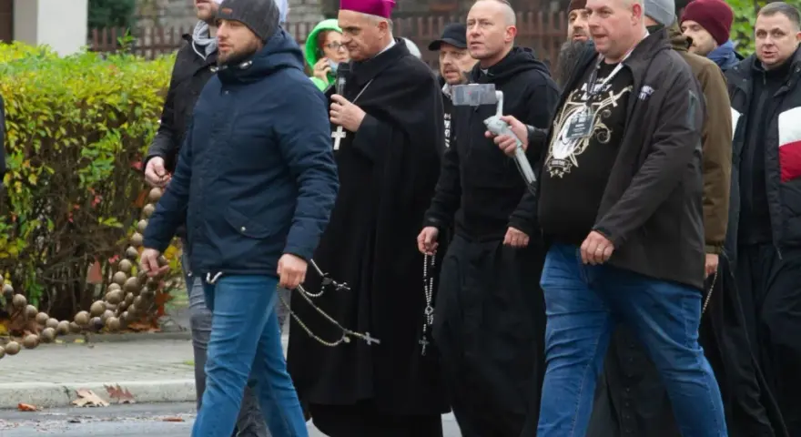 Grupa mężczyzn, w tym biskup, idzie ulicą. Niektórzy niosą różańce, jak rycerze Maryi.