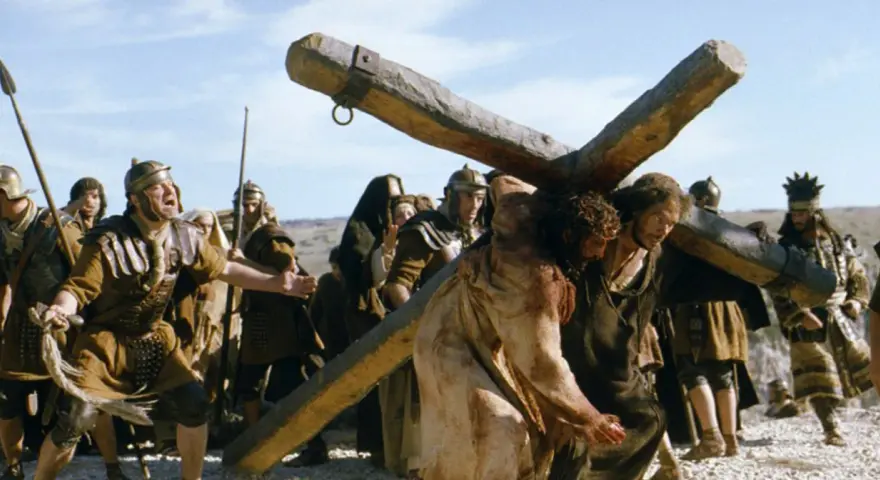 Scena z filmów chrześcijańskich: Jezus dźwigający krzyż, otoczony przez żołnierzy.