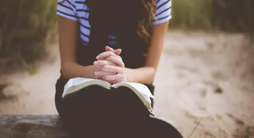 Kobieta z dłońmi złożonymi nad otwartą Biblią. To jej modlitwa o dobry dzień w pracy.