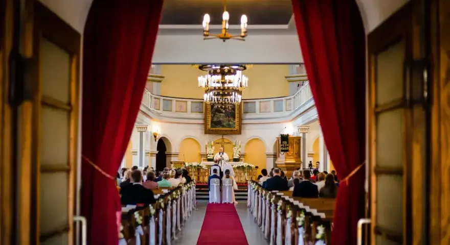 Ślub w kościele. Para młoda przed ołtarzem, ksiądz udziela im błogosławieństwa. Wszyscy zgromadzeni są chrześcijanami, a ten konkretny obrządek jest katolicki.