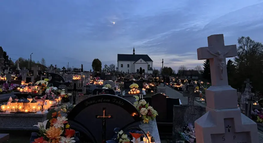 Cmentarz nocą, pełen płonących zniczy i kwiatów. W oddali kościół, a na niebie księżyc. Modlitwa świętej Gertrudy w ciszy zadumy.