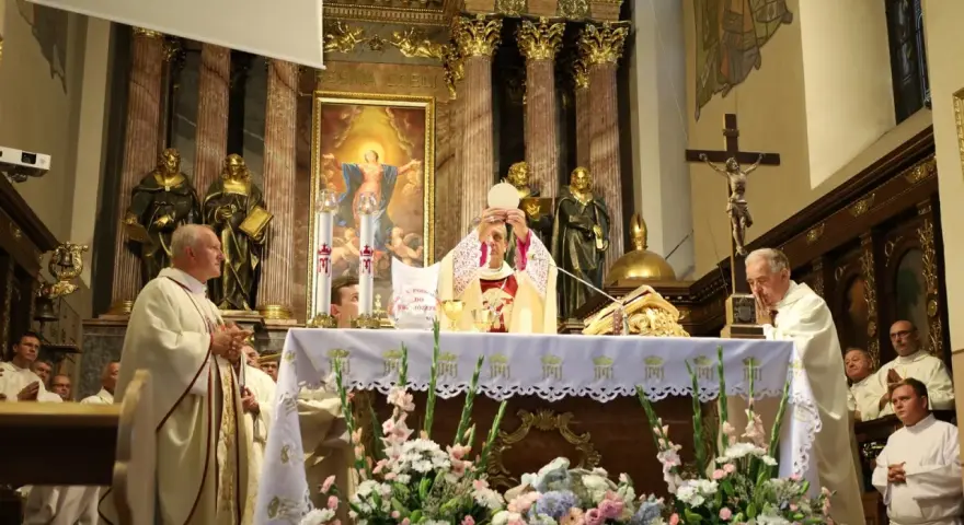 Uroczysta msza święta w kościele. Kapłan podnosi hostię, symbolizując piękna modlitwę do Boga. W tle złote zdobienia i obrazy.
