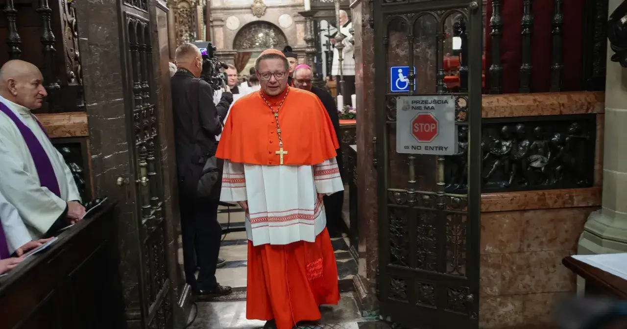 Arcybiskup krakowski w stroju kardynalskim przechodzi przez zabytkowe drzwi.