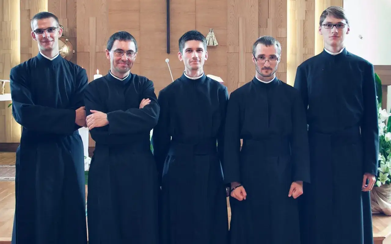 Pięciu młodych mężczyzn w czarnych sutannach, przyszli jezuici, pozuje do zdjęcia w kościele.
