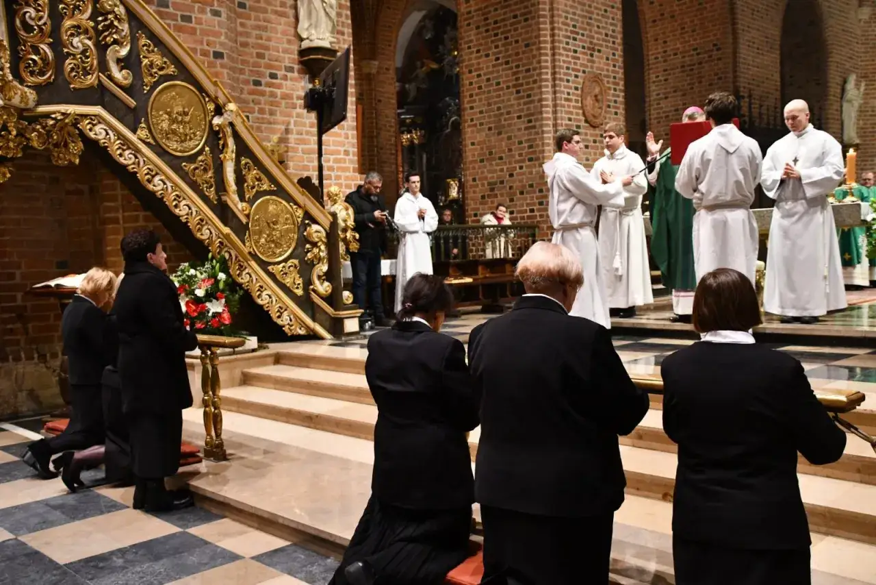 Uroczystość kościelna, gdzie kobiety w czerni klęczą przed ołtarzem, a duchowni w białych szatach celebrują. Wśród nich, być może, wdowa konsekrowana.